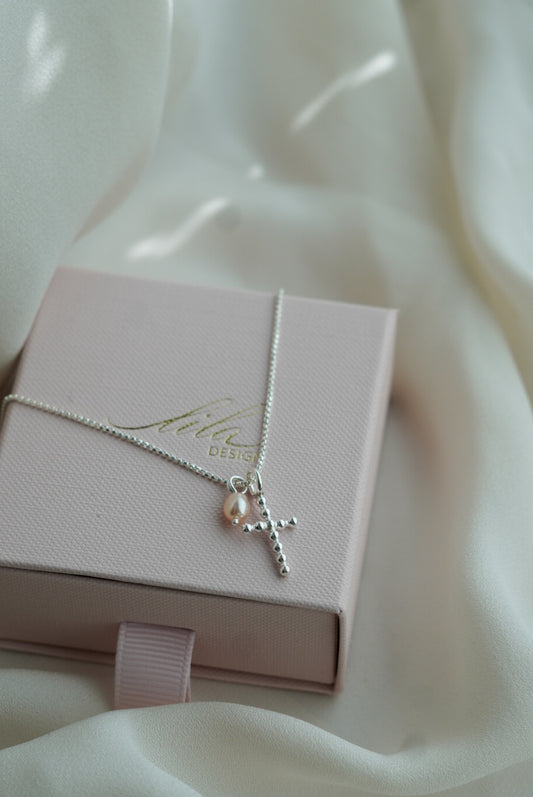 vaaleanpunaisella helmellä oleva rippiristi_työlle rippiristi_hopeinen rippiritsi ja helmi_helmi ja risti koru
